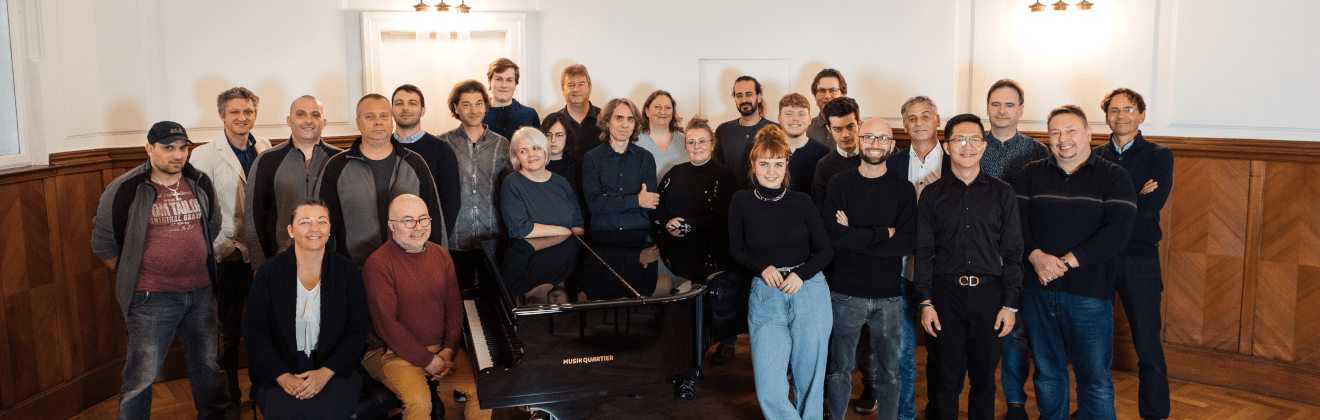 Ihr Team der Klavier Galerie - Gruppenfoto der Belegschaft, gut 25 Menschen stehen hinter einen Flügel